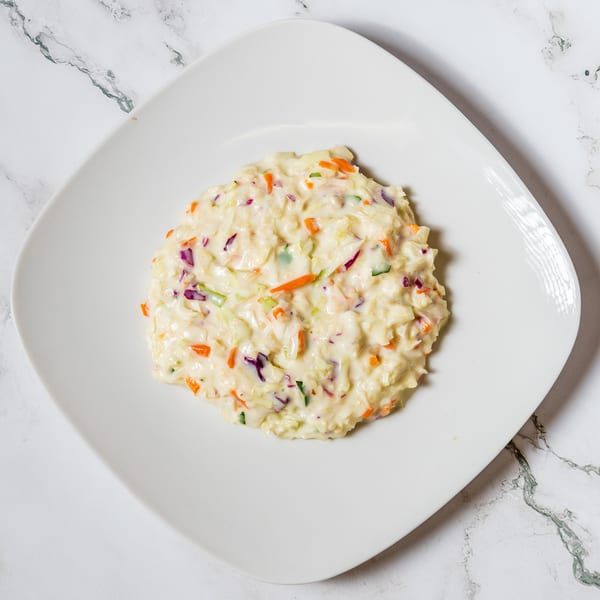 Creamy coleslaw with shredded cabbage, carrots, and red onion on a white square plate.