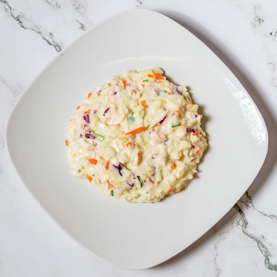 Creamy coleslaw with shredded cabbage, carrots, and red onion on a white square plate.