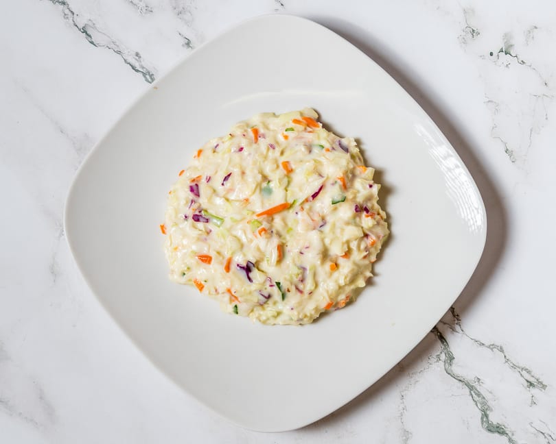 Creamy coleslaw with shredded cabbage, carrots, and red onion on a white square plate.