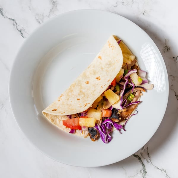 A single taco filled with pineapple, red cabbage, and other vegetables on a white plate.