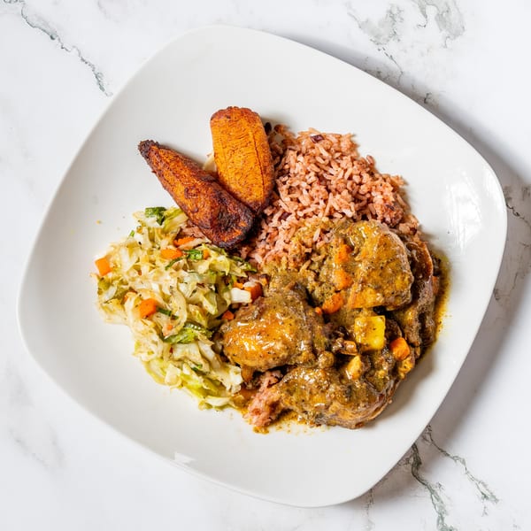 Curry chicken with rice and peas, fried plantains, and steamed cabbage on a white plate.