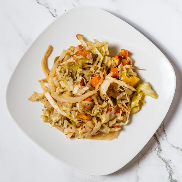 A white square plate filled with sautéed cabbage, carrots, and onions on a marble surface.
