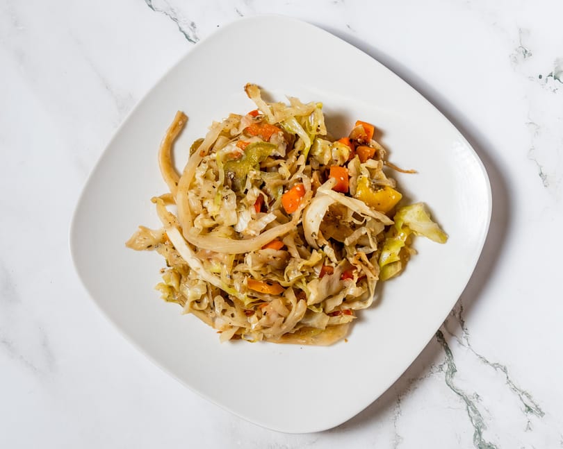 A white square plate filled with sautéed cabbage, carrots, and onions on a marble surface.