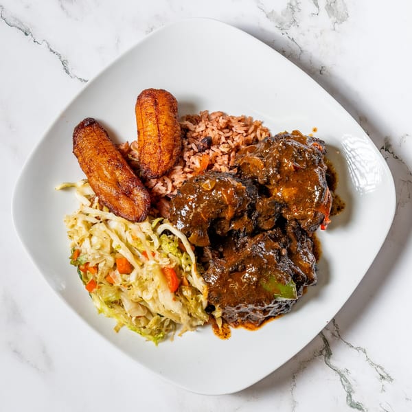 Oxtail stew with rice and peas, fried plantains, and steamed cabbage on a white plate.