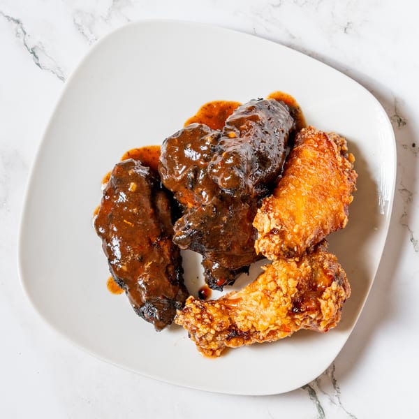 A white plate holds two dark, saucy chicken wings and two crispy, golden-brown chicken wings.