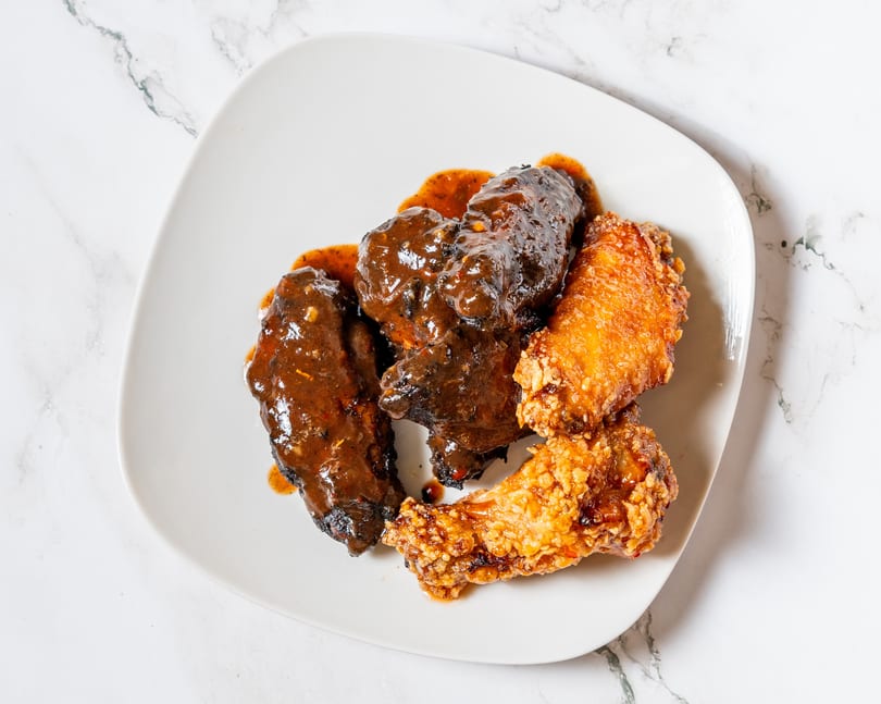A white plate holds two dark, saucy chicken wings and two crispy, golden-brown chicken wings.