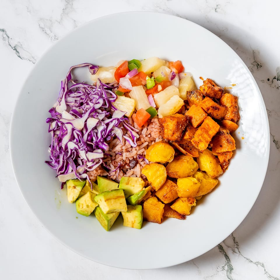 A colorful bowl with red cabbage, rice, avocado, pineapple salsa, and fried plantains.