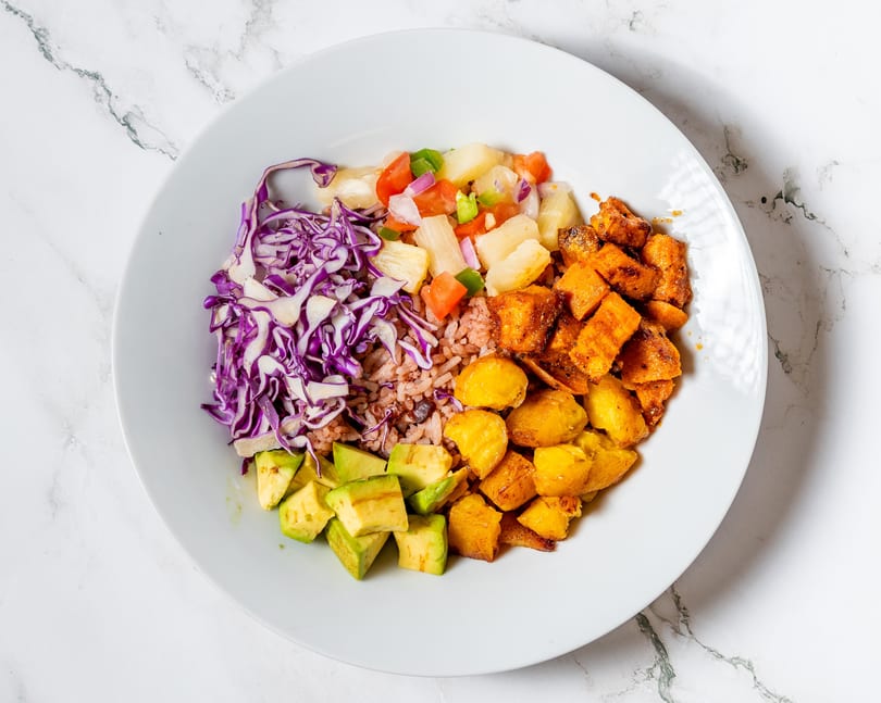 A colorful bowl with red cabbage, rice, avocado, pineapple salsa, and fried plantains.
