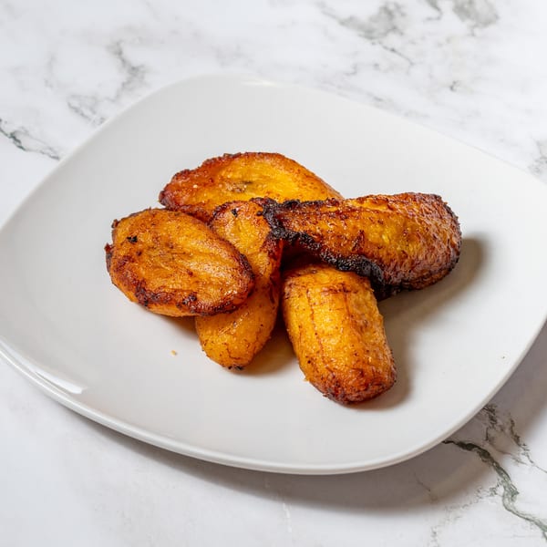 Golden brown fried plantains, some with dark crispy edges, on a white plate.
