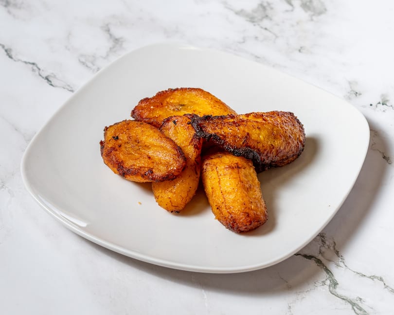 Golden brown fried plantains, some with dark crispy edges, on a white plate.