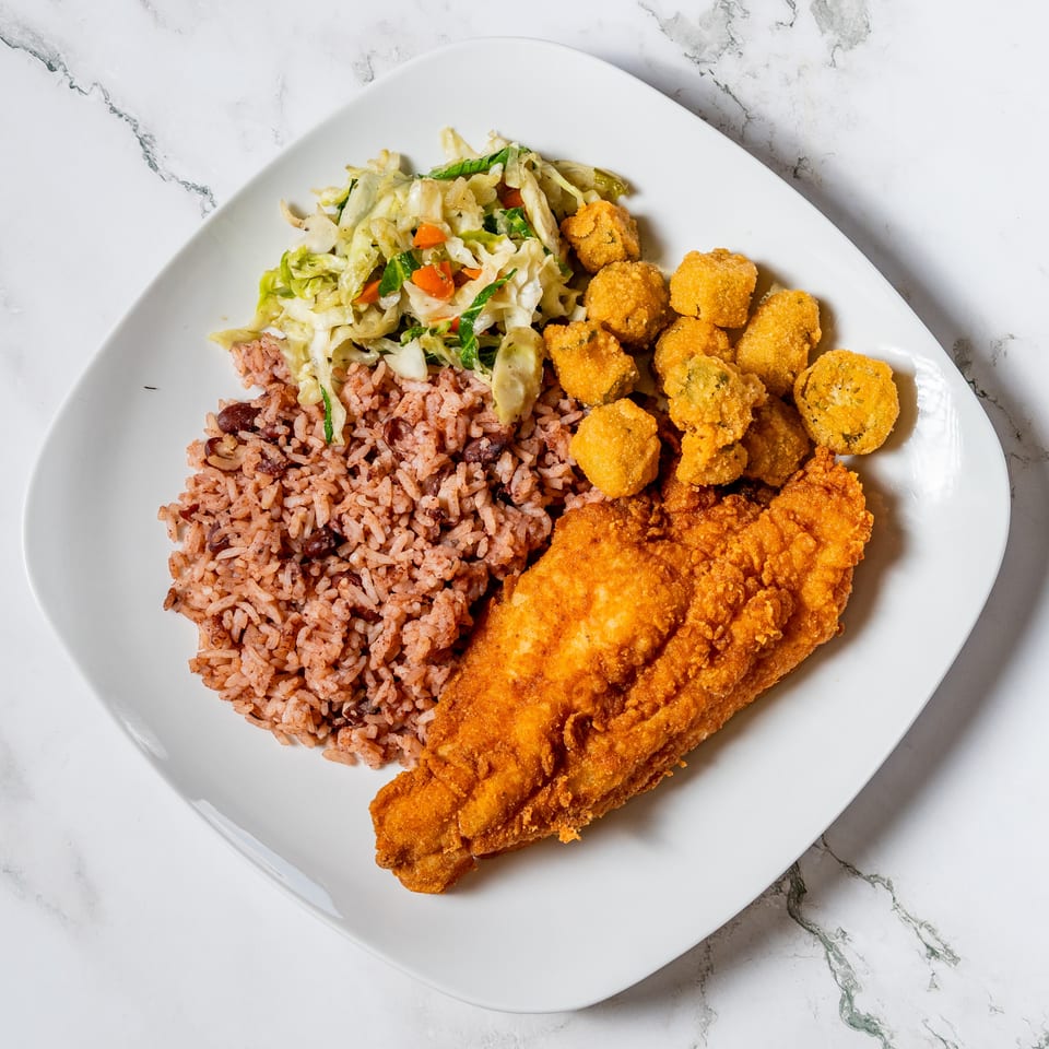 Fried fish fillet, rice and beans, fried okra, and coleslaw on a white plate.