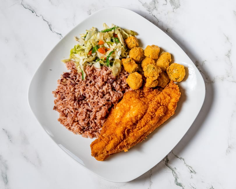Fried fish fillet, rice and beans, fried okra, and coleslaw on a white plate.